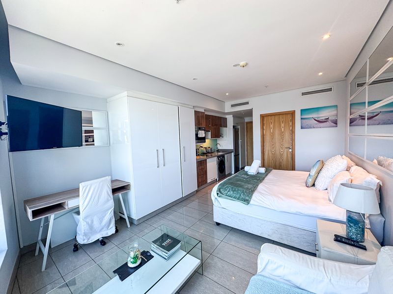 A modern open-plan studio apartment featuring a kitchenette, built-in cabinetry, tiled flooring, and recessed lighting, offering a functional and well-maintained living space.