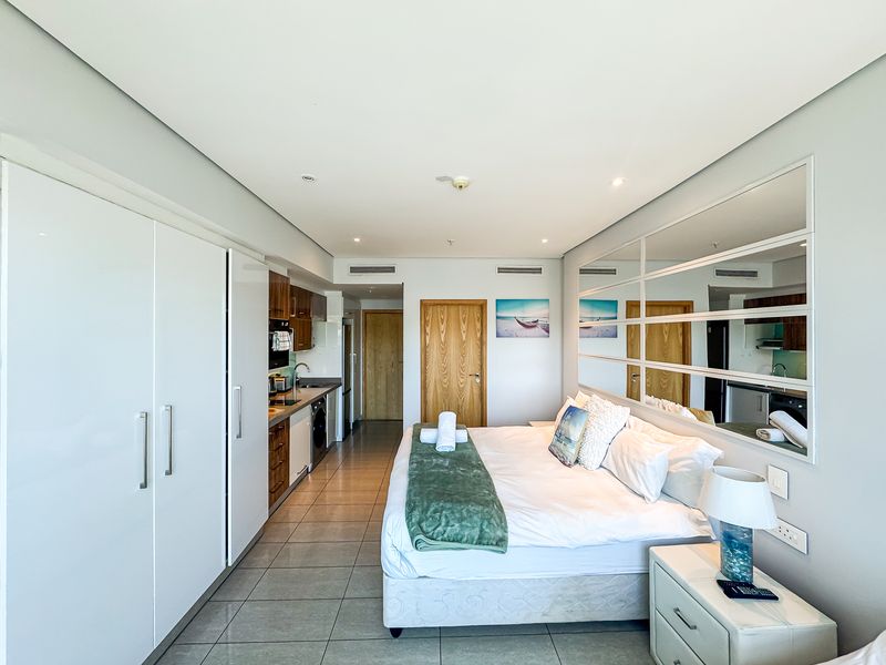 Modern open-plan studio apartment featuring a compact kitchen, built-in storage, tiled flooring, and a large mirrored feature wall.