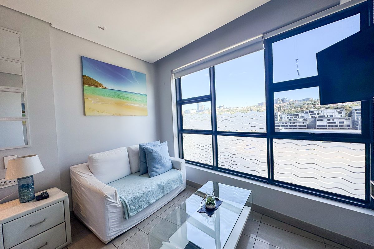 A bright living room featuring large aluminium-framed windows with city views, tiled flooring, and modern recessed lighting.