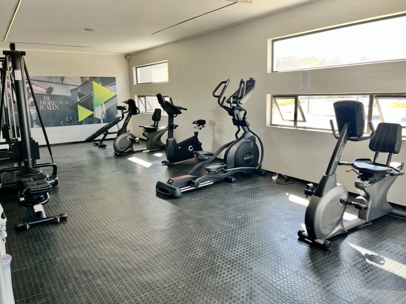 A well-maintained apartment gym facility featuring durable rubberized flooring and multiple horizontal windows providing natural light.