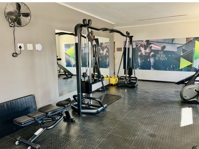 A functional apartment gym space featuring durable rubber flooring, wall-mounted mirrors, and a wall-mounted fan for ventilation.