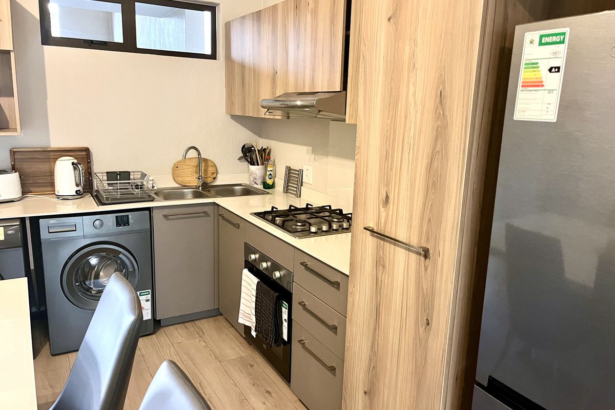 Modern kitchen featuring wood-finish cabinetry, integrated gas hob, built-in oven, extractor fan, and a stainless steel sink with tiled backsplash.