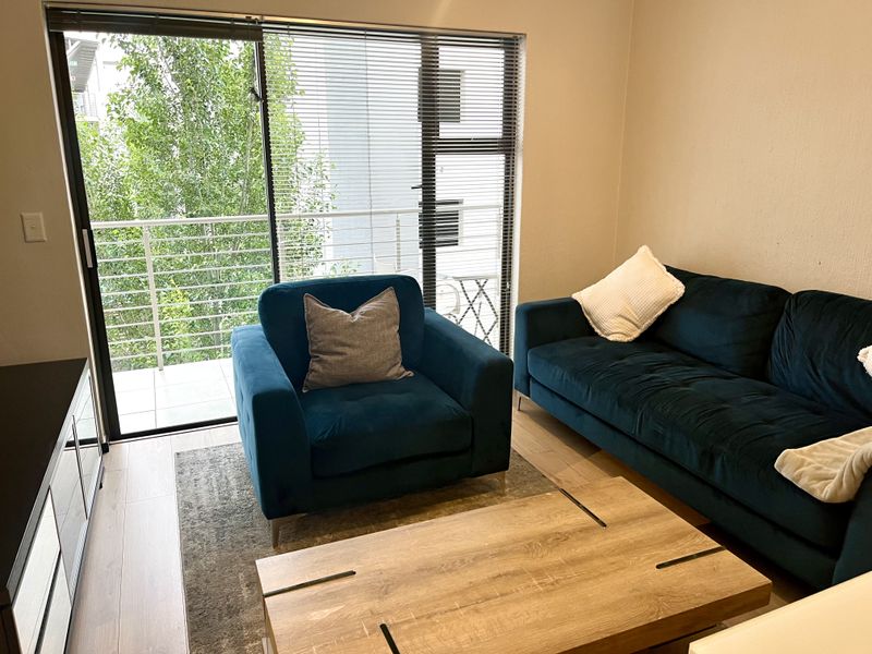 A well-lit living room featuring laminate flooring and a large sliding glass door providing direct access to a private balcony.