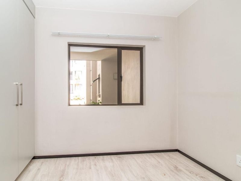 A clean, empty bedroom featuring light-toned laminate flooring, neutral walls, and built-in cupboards, offering a blank canvas for personalization.