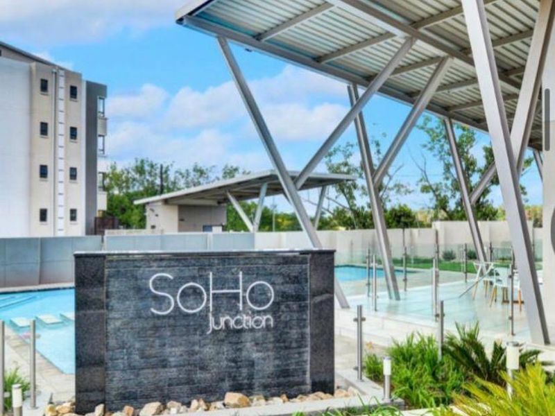 Modern communal pool area at SoHo Junction featuring a covered patio, glass balustrades, and a decorative water feature.