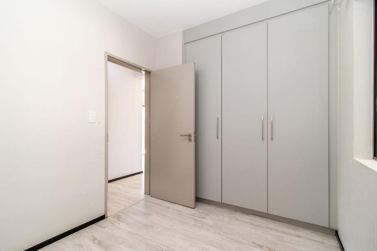 A clean, empty bedroom featuring modern light-toned laminate flooring and built-in cupboards with a neutral finish.