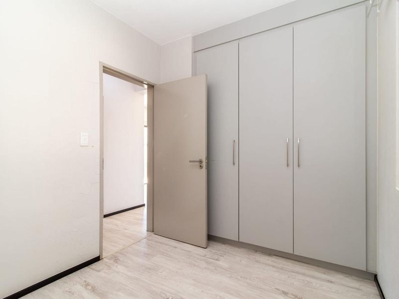 A clean, empty bedroom featuring modern light-toned laminate flooring and built-in cupboards with a neutral finish.