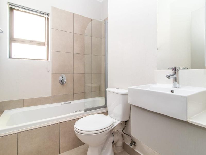 A clean and modern bathroom featuring a bathtub with a glass shower screen, a wall-mounted vanity basin, and neutral wall tiling.