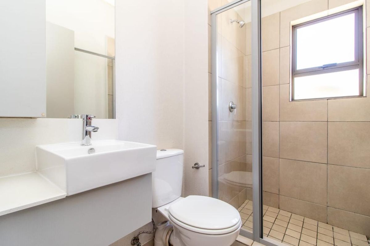 A clean, modern bathroom featuring a glass-enclosed shower, wall-mounted basin, and toilet with neutral tiling.