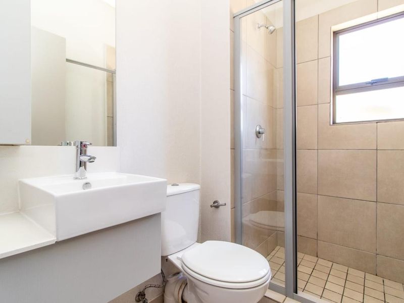 A clean, modern bathroom featuring a glass-enclosed shower, wall-mounted basin, and toilet with neutral tiling.