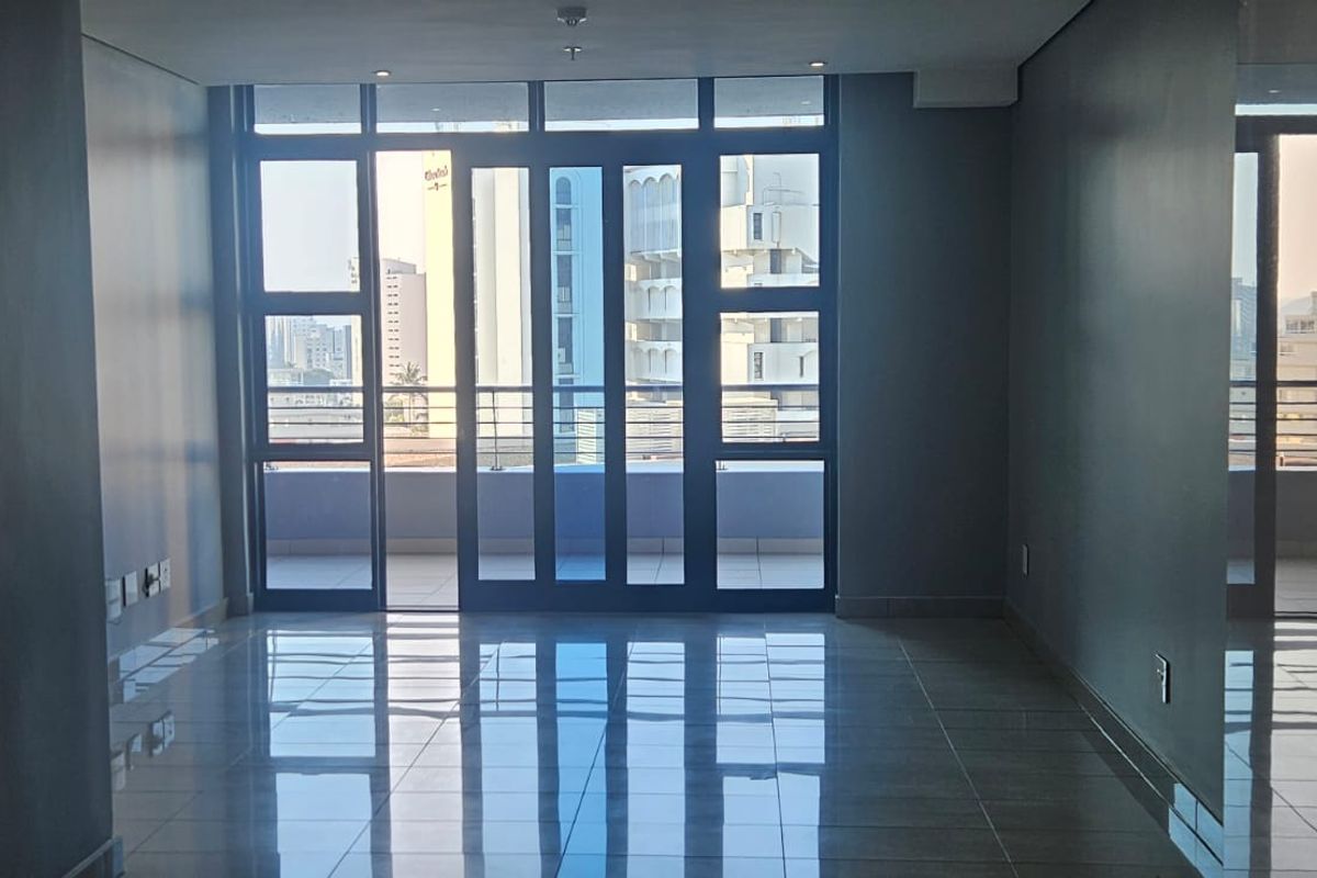 An empty, well-maintained living area featuring polished tiled floors and large glass sliding doors that provide access to a balcony with city views.