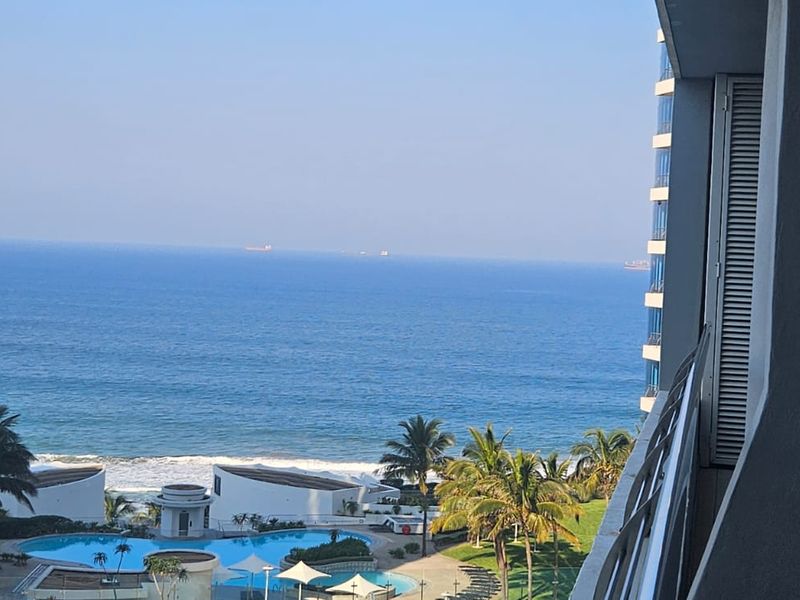 Elevated view overlooking the swimming pool area and the ocean from a private apartment balcony.