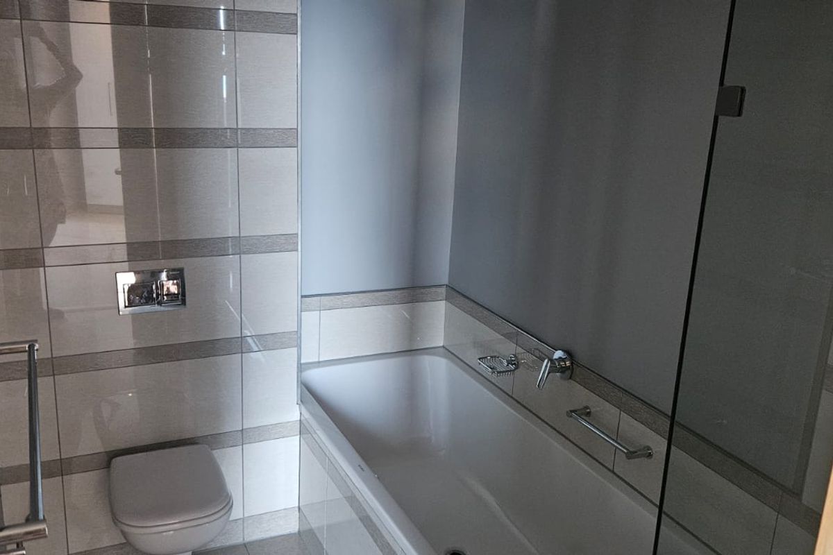 Modern bathroom featuring a wall-mounted toilet, a bathtub with chrome fixtures, and a glass shower screen, finished with neutral ceramic wall tiling.