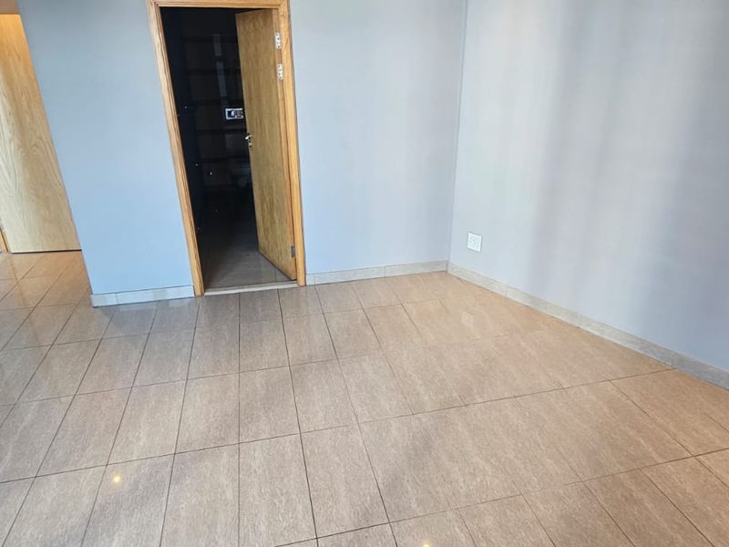 A bright, empty living area featuring neutral grey walls, modern tiled flooring, and clean wooden door frames, ready for personalization.