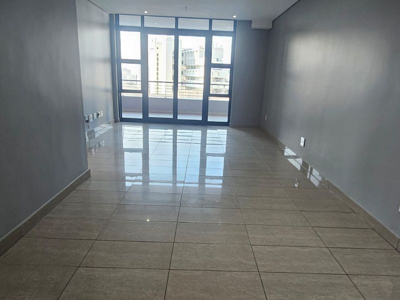 A spacious, empty living area featuring neutral grey walls, polished tiled flooring, and large sliding glass doors providing natural light and balcony access.
