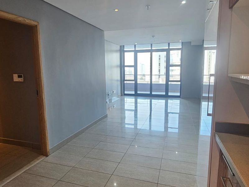 Spacious open-plan living area featuring polished tile flooring, recessed lighting, and large sliding glass doors leading to a balcony.