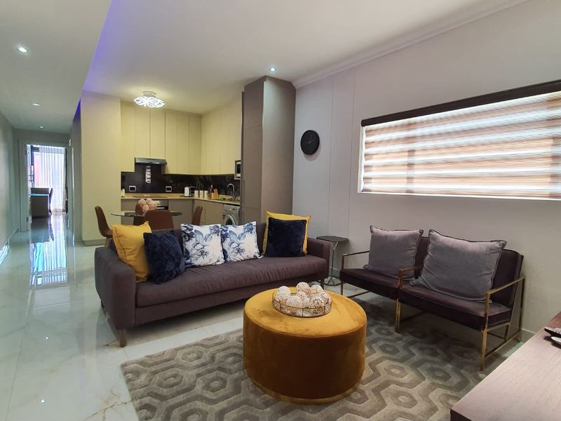 Modern open-plan living area featuring tiled floors, recessed lighting, and a compact kitchen with built-in cabinetry and integrated appliances.