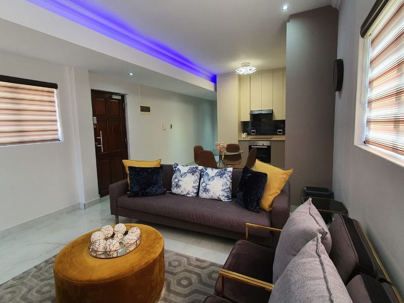 Modern open-plan living area featuring recessed LED lighting, tiled floors, and a compact, well-appointed kitchen with built-in appliances.