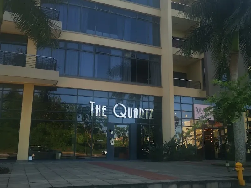 Front elevation of The Quartz apartment building featuring a modern glass facade, paved entrance area, and multi-level balconies.