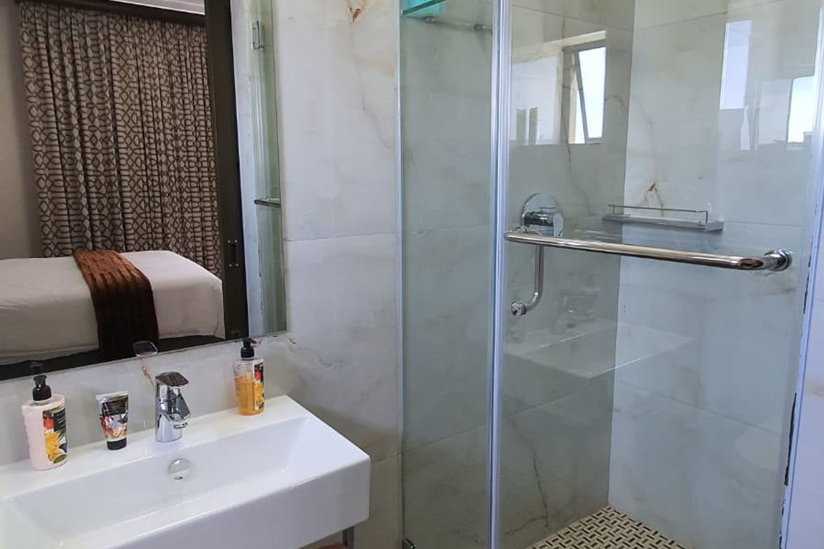 Modern bathroom featuring a wall-mounted basin, glass-enclosed shower with patterned floor tiles, and elegant marble-look wall tiling.