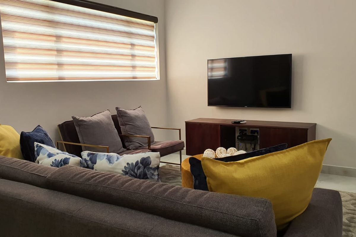 A well-maintained living room featuring tiled flooring, neutral walls, and modern roller blinds, providing a clean and comfortable space.