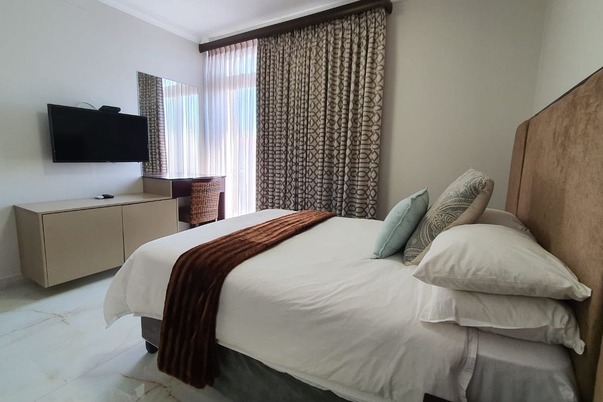 A well-maintained bedroom featuring tiled flooring, built-in vanity unit, wall-mounted mirror, and floor-to-ceiling curtains providing access to natural light.