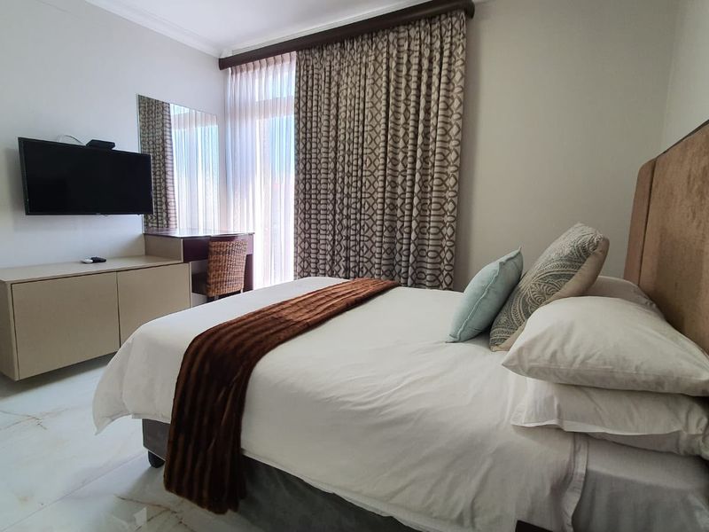 A well-maintained bedroom featuring tiled flooring, built-in vanity unit, wall-mounted mirror, and floor-to-ceiling curtains providing access to natural light.