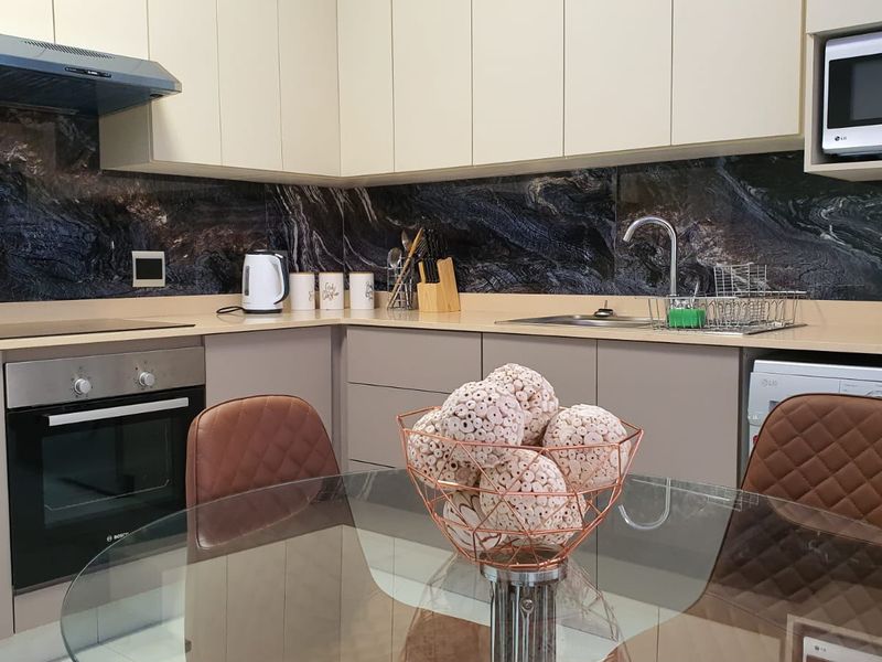 Modern kitchen featuring sleek cabinetry, stone splashback, built-in oven, extractor fan, and integrated microwave with ample counter space.