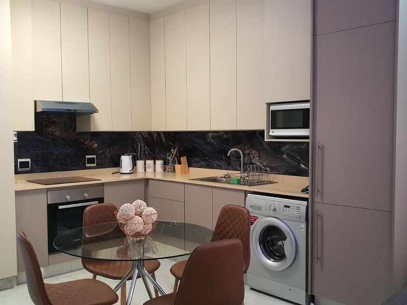 Modern kitchen featuring sleek handleless cabinetry, dark stone splashback, integrated appliances including an oven, microwave, and washing machine, and a clean, contemporary finish.