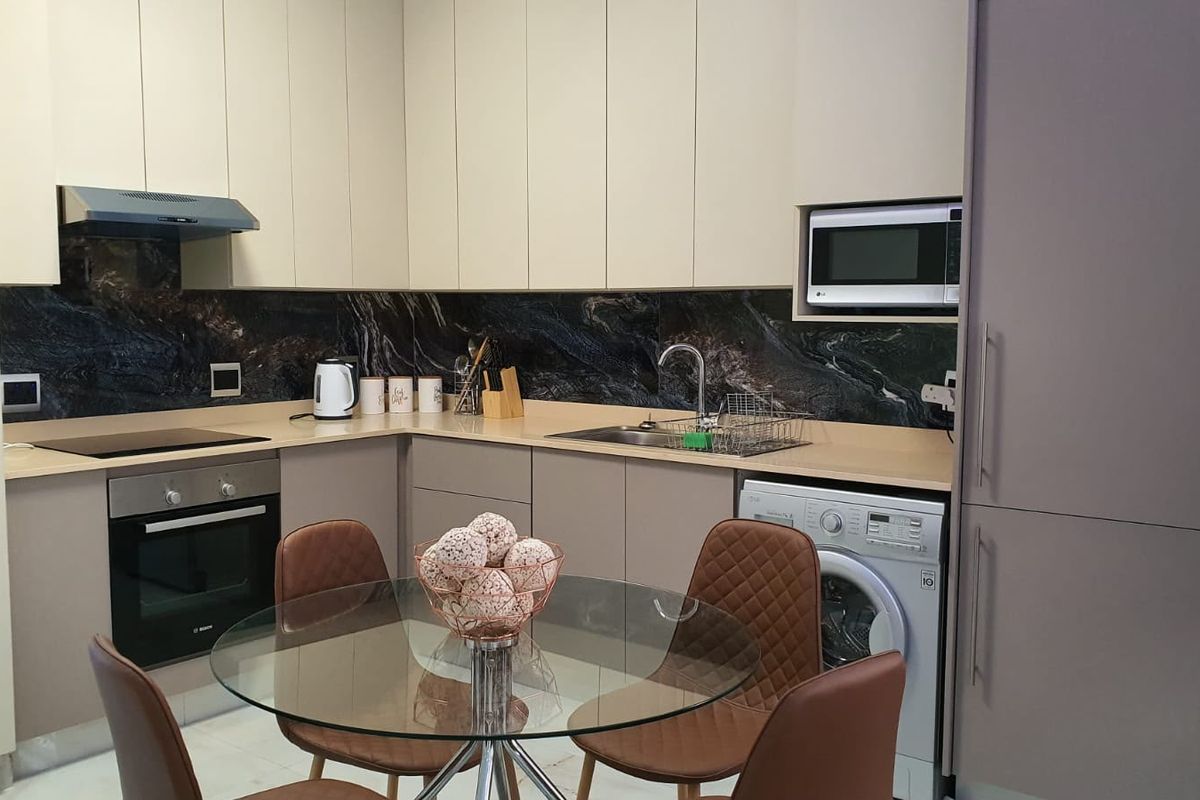 Modern kitchen featuring sleek handleless cabinetry, stone splashback, integrated appliances including an oven, hob, microwave, and washing machine, with ample counter space.