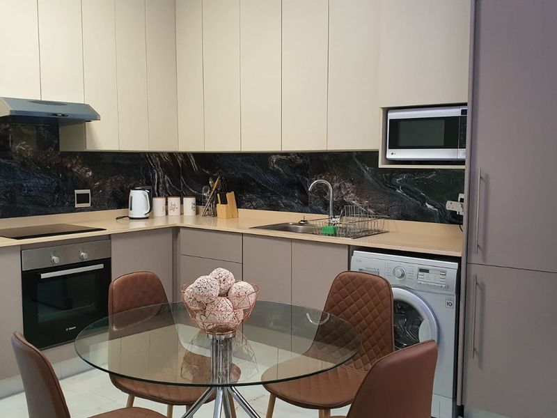 Modern kitchen featuring sleek handleless cabinetry, stone splashback, integrated appliances including an oven, hob, microwave, and washing machine, with ample counter space.