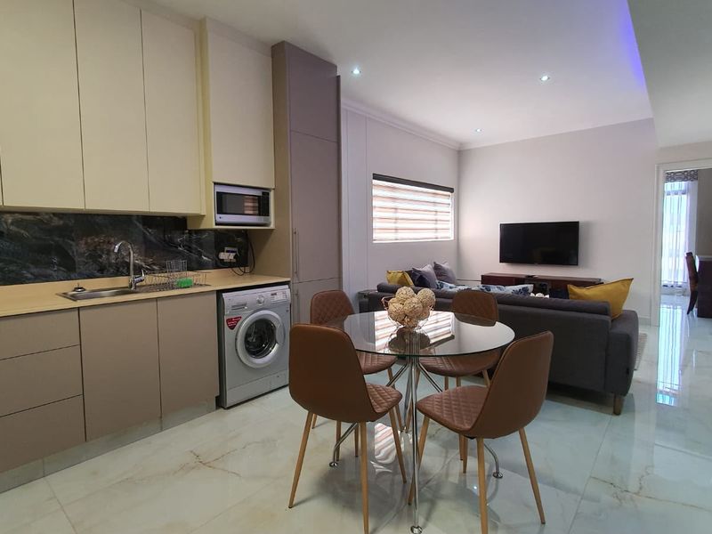 Modern open-plan living area featuring a sleek kitchen with integrated appliances, stone-look backsplash, and polished tiled flooring throughout.