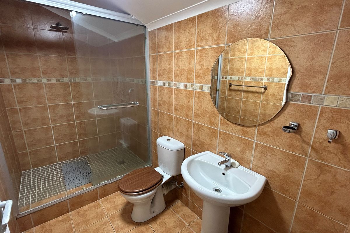 A functional bathroom featuring a walk-in shower with glass enclosure, pedestal basin, and toilet, finished with warm-toned ceramic wall and floor tiles.