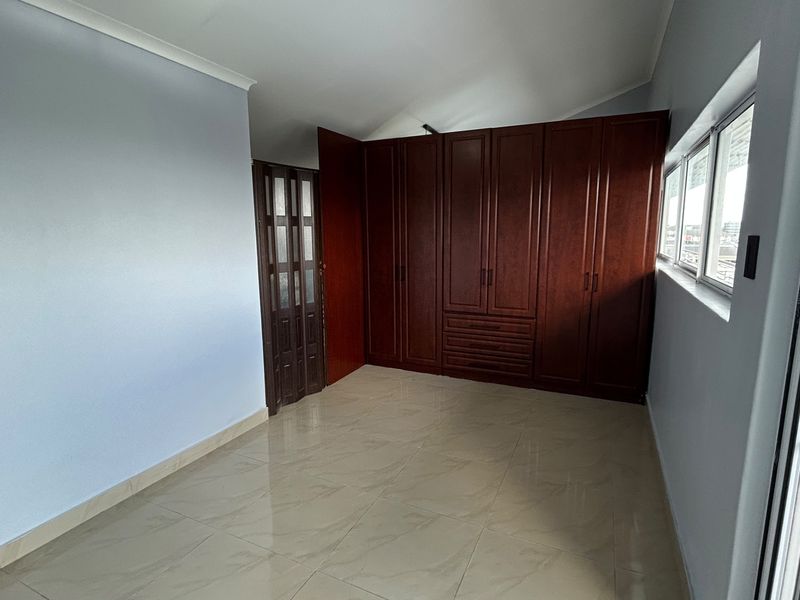 A bright, empty bedroom featuring polished tiled flooring, neutral walls, and extensive dark wood built-in cabinetry with ample storage space.