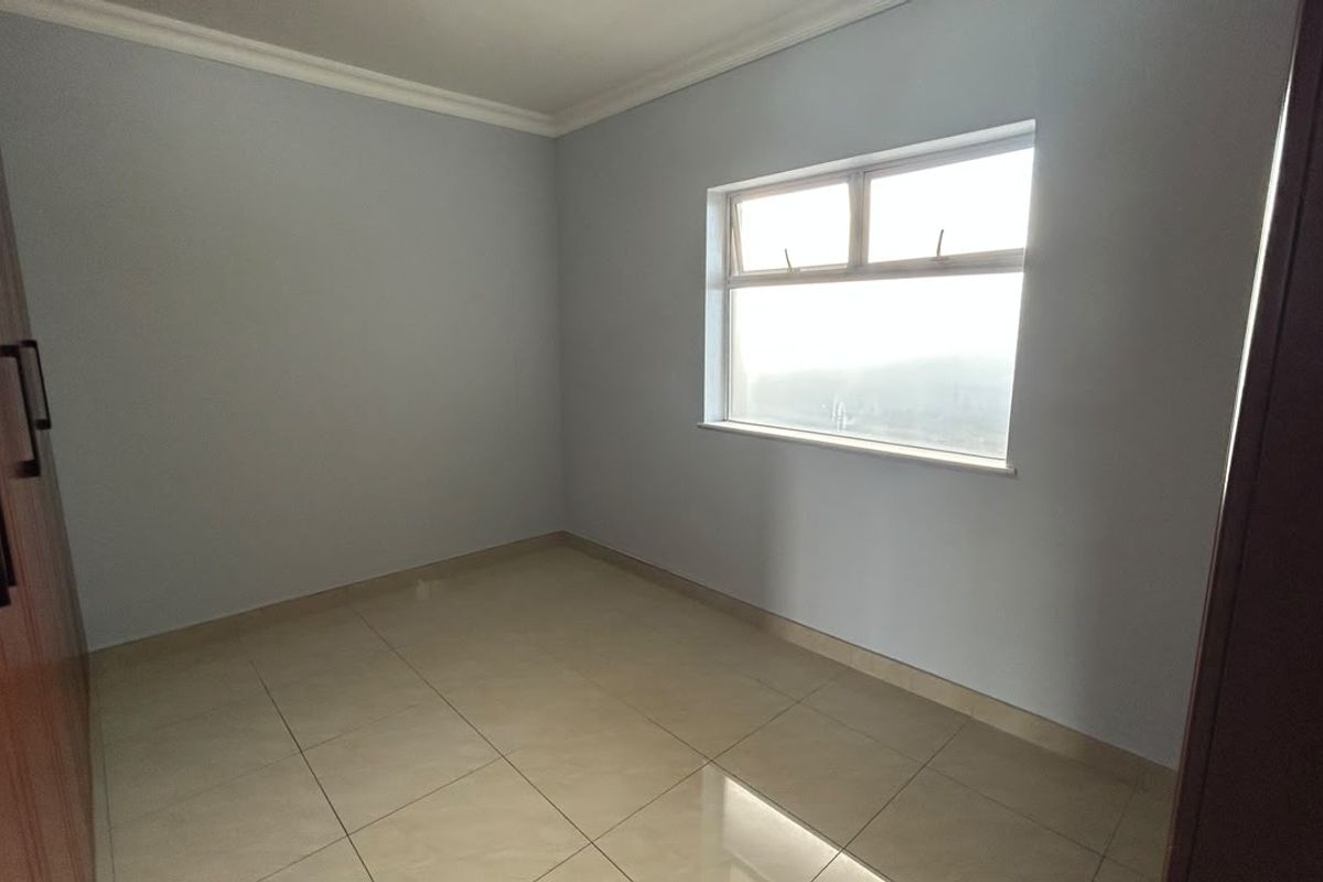 A clean, empty bedroom featuring neutral tiled flooring, built-in cupboards, and classic ceiling cornicing, offering a blank canvas for personalization.