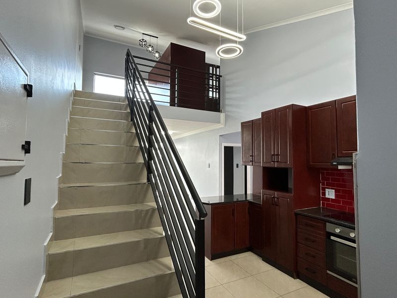 Open-plan living area featuring a staircase leading to a mezzanine level, complemented by a modern kitchen with dark wood cabinetry and granite countertops.