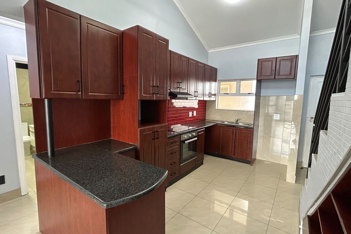 A clean, functional kitchen featuring dark wood cabinetry, granite countertops, built-in oven and hob, and tiled flooring with a vaulted ceiling.