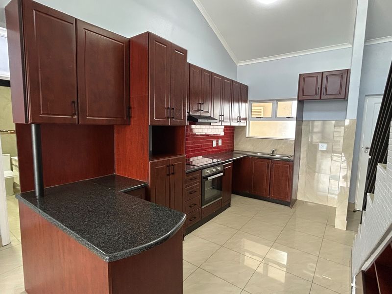 A clean, functional kitchen featuring dark wood cabinetry, granite countertops, built-in oven and hob, and tiled flooring with a vaulted ceiling.