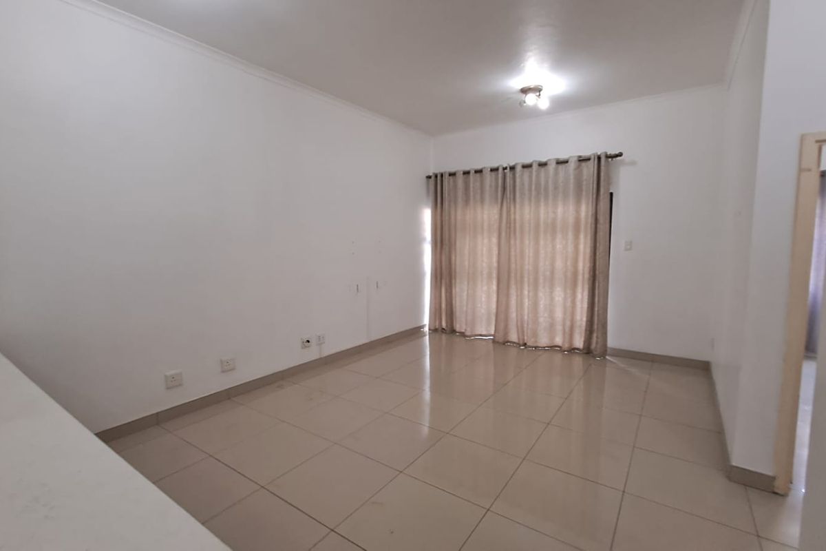 A spacious, empty living room featuring neutral tiled flooring, white walls, and large window curtains, providing a blank canvas for interior design.