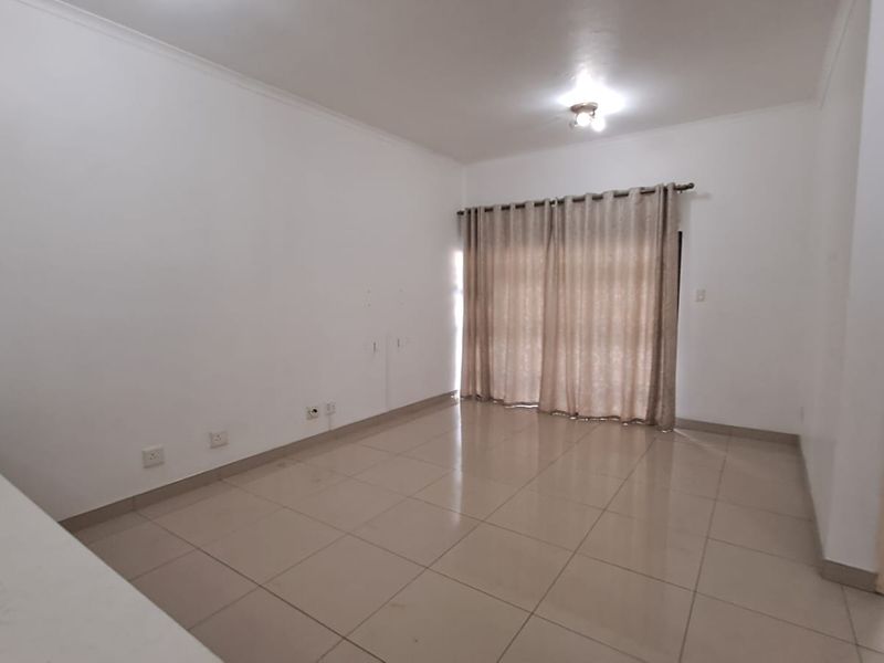 A spacious, empty living room featuring neutral tiled flooring, white walls, and large window curtains, providing a blank canvas for interior design.