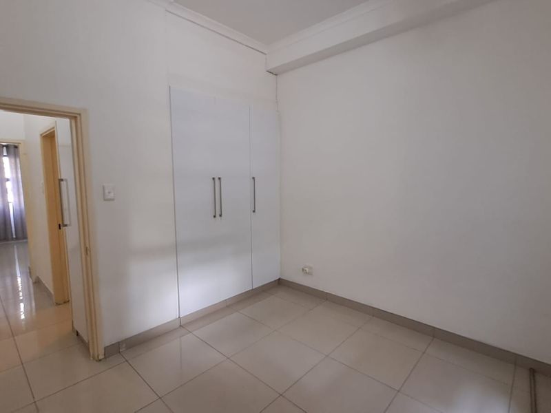 A bright, empty bedroom featuring neutral tiled flooring and white built-in cupboards, offering a clean and versatile space ready for personalization.