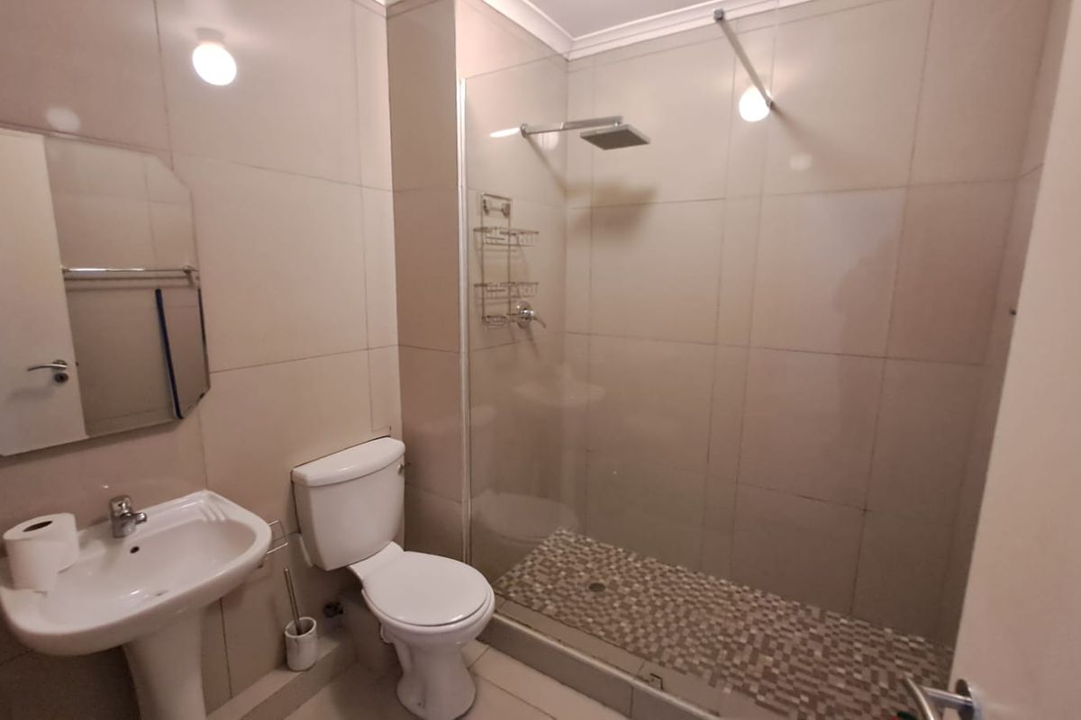A functional bathroom featuring a pedestal basin, toilet, and a walk-in shower with a glass screen and rainfall shower head.