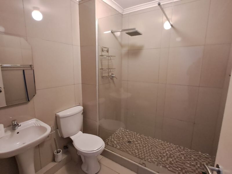 A functional bathroom featuring a pedestal basin, toilet, and a walk-in shower with a glass screen and rainfall shower head.
