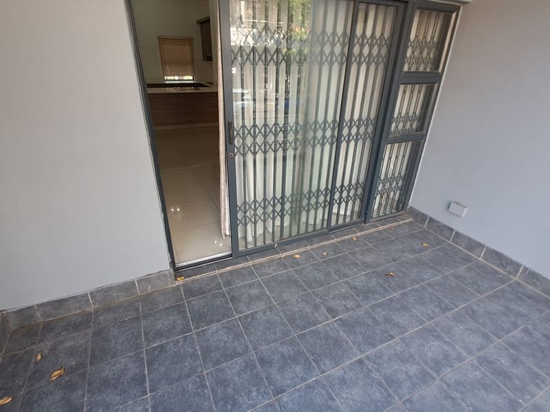 A covered balcony featuring dark tiled flooring and a secure sliding glass door entrance leading into the apartment interior.