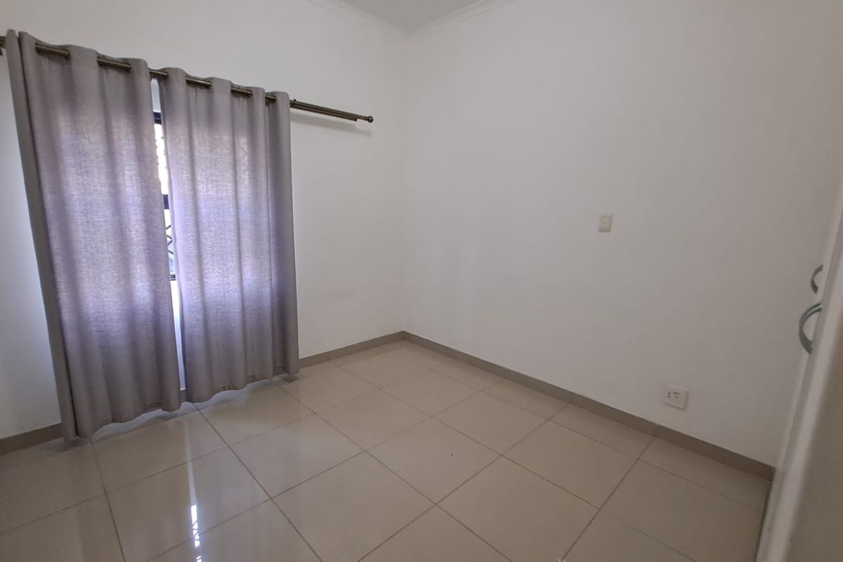A clean, empty bedroom featuring neutral tiled flooring, white walls, and a fitted curtain rod, providing a blank canvas for personalization.