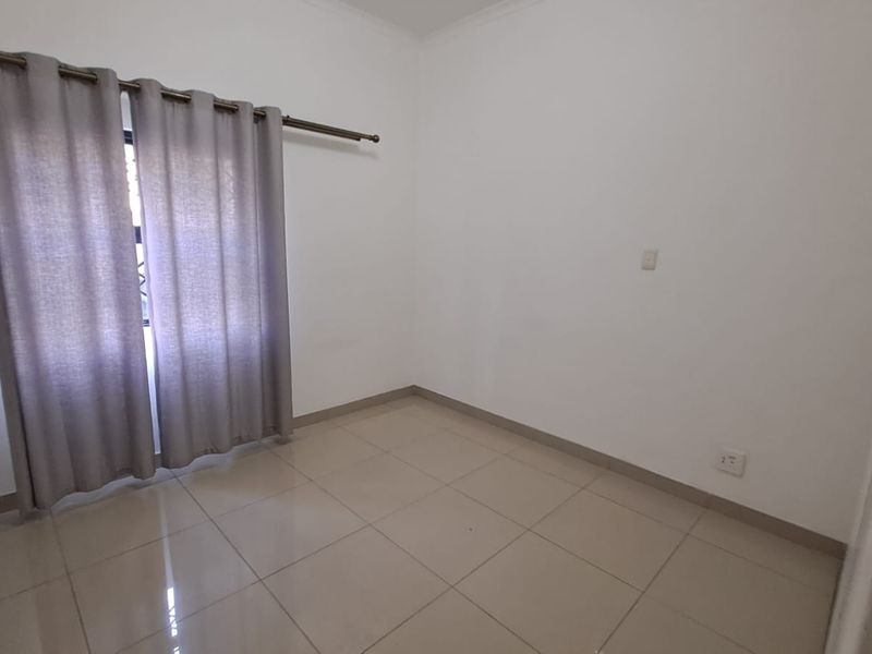 A clean, empty bedroom featuring neutral tiled flooring, white walls, and a fitted curtain rod, providing a blank canvas for personalization.