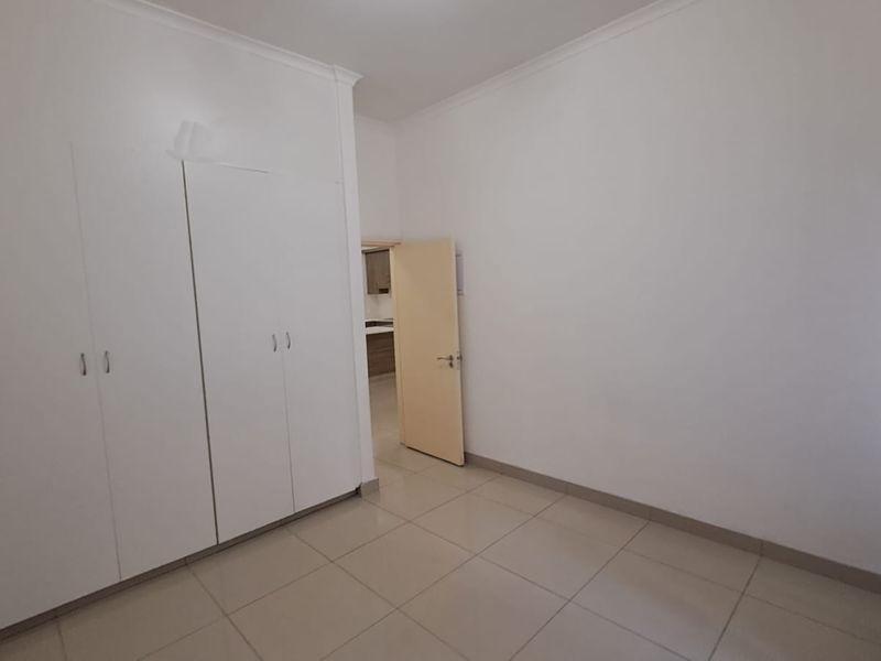 A bright, empty bedroom featuring neutral tiled flooring and ample built-in cupboard storage space.