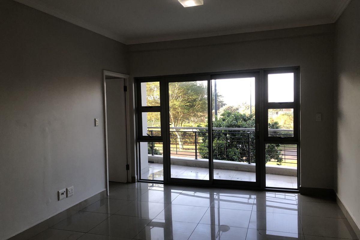An empty living room featuring tiled flooring, a ceiling light fixture, and a large sliding glass door providing access to a balcony.