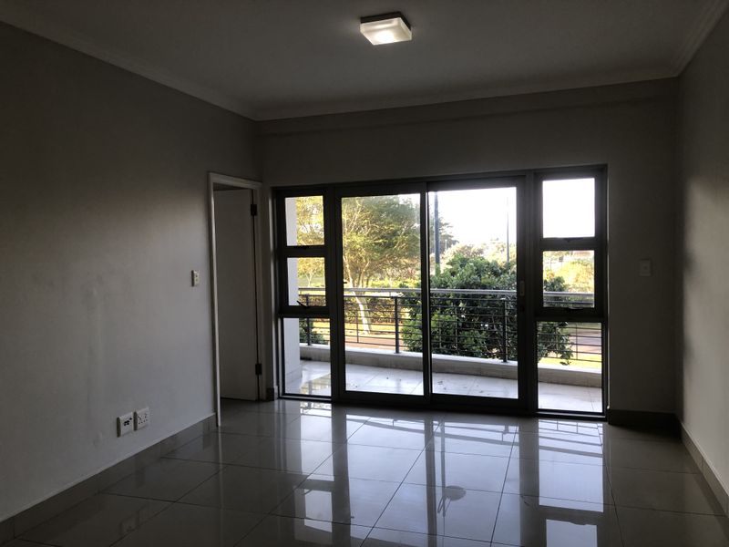 An empty living room featuring tiled flooring, a ceiling light fixture, and a large sliding glass door providing access to a balcony.
