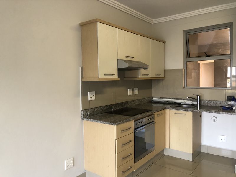 A compact, modern kitchen featuring light wood cabinetry, granite countertops, built-in oven, electric hob, and tiled splashback in a clean, neutral space.